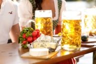 Two beer mugs, radishes and cheese are lying on a table in a beer garden in Munich.