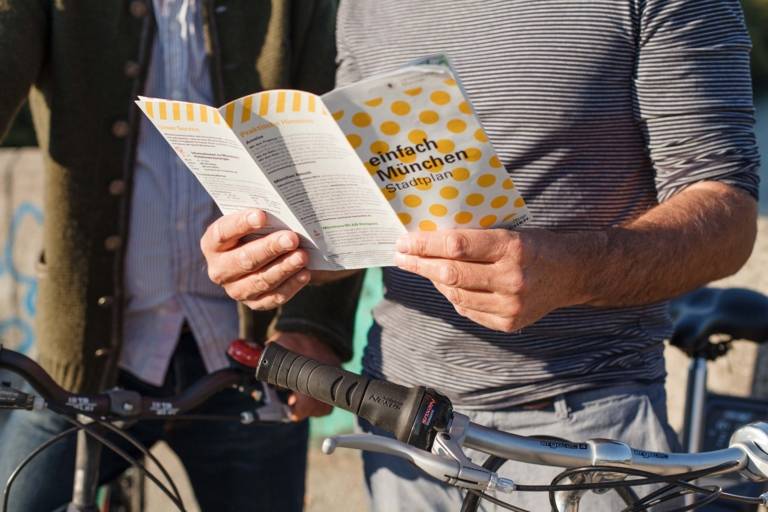 A man is holding a city map in his hands. A bike is besides him.
