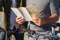 A man is holding a city map in his hands. A bike is besides him.