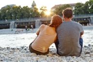 A couple is sitting on stones and is looking to the water of the Isar River in Munich.