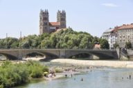 People swimming and sun bathing at the Isar river in München with the church St Maximilian in the background.