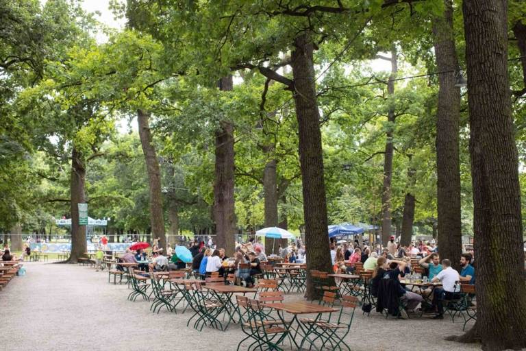 People are sitting under chestnut trees in the beer garden Hirschgarten in Munich.