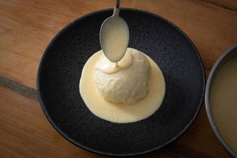 A Dampfnudel with vanilla sauce on a dark plate.