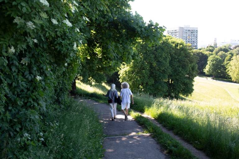 A couple walks down the hill along green meadows on a path in Luitpold Park.