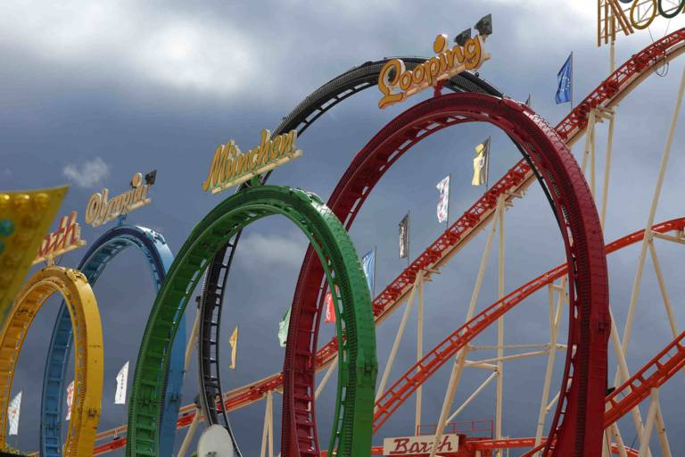 Loops of the roller coaster in the colors yellow, blue-red and green with writing against the blue sky.