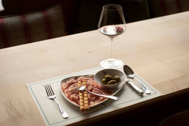 A glass of wine and a plate of ham and olives in Geisels Vinothek in Munich