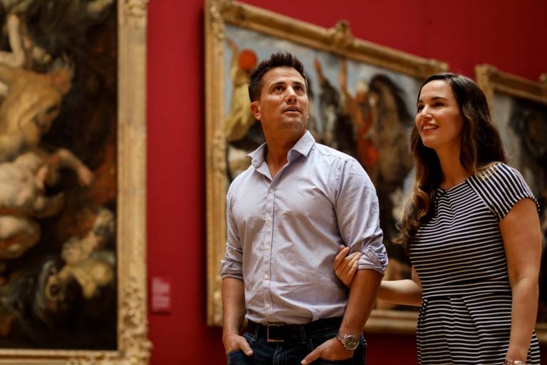 A couple is walking arm in arm through the Alte Pinakothek in Munich and is looking at paintings.