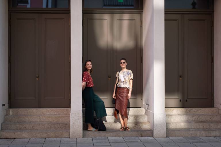 Two women stand in front of three large wooden doors in Munich.